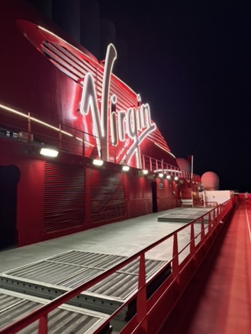 The illuminated Virgin script sign glowing red on the ship's exterior deck at night.